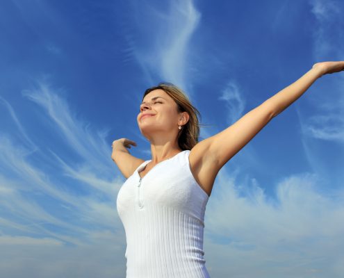Young woman with open hands standing against the beautiful sky.