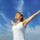Young woman with open hands standing against the beautiful sky.