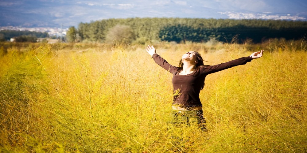woman in field smiling with hands in air