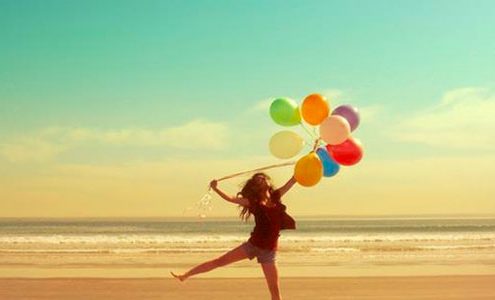 Happy girl holding balloons on the beach